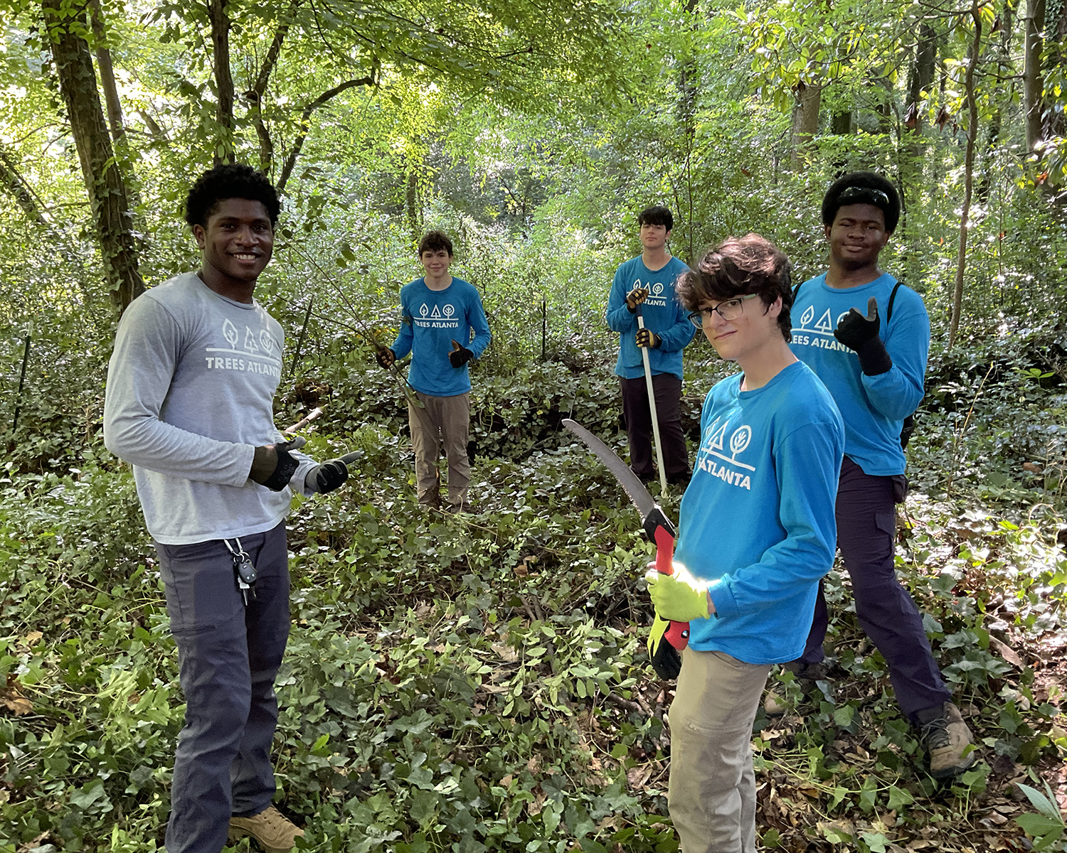 Trees Atlanta Youth Tree Team Mentor, Drew Kenner (L), Leader-In-Training Liam Rocks (R foreground), and members of the Youth Tree Team take a pause from tackling cherry laurel to smile for the camera.